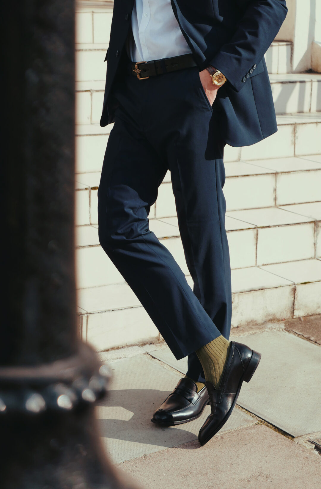 A Man leans against a lamp post in a navy blue suit and olive green cotton socks by London Sock Company and stylist Michael Fisher.