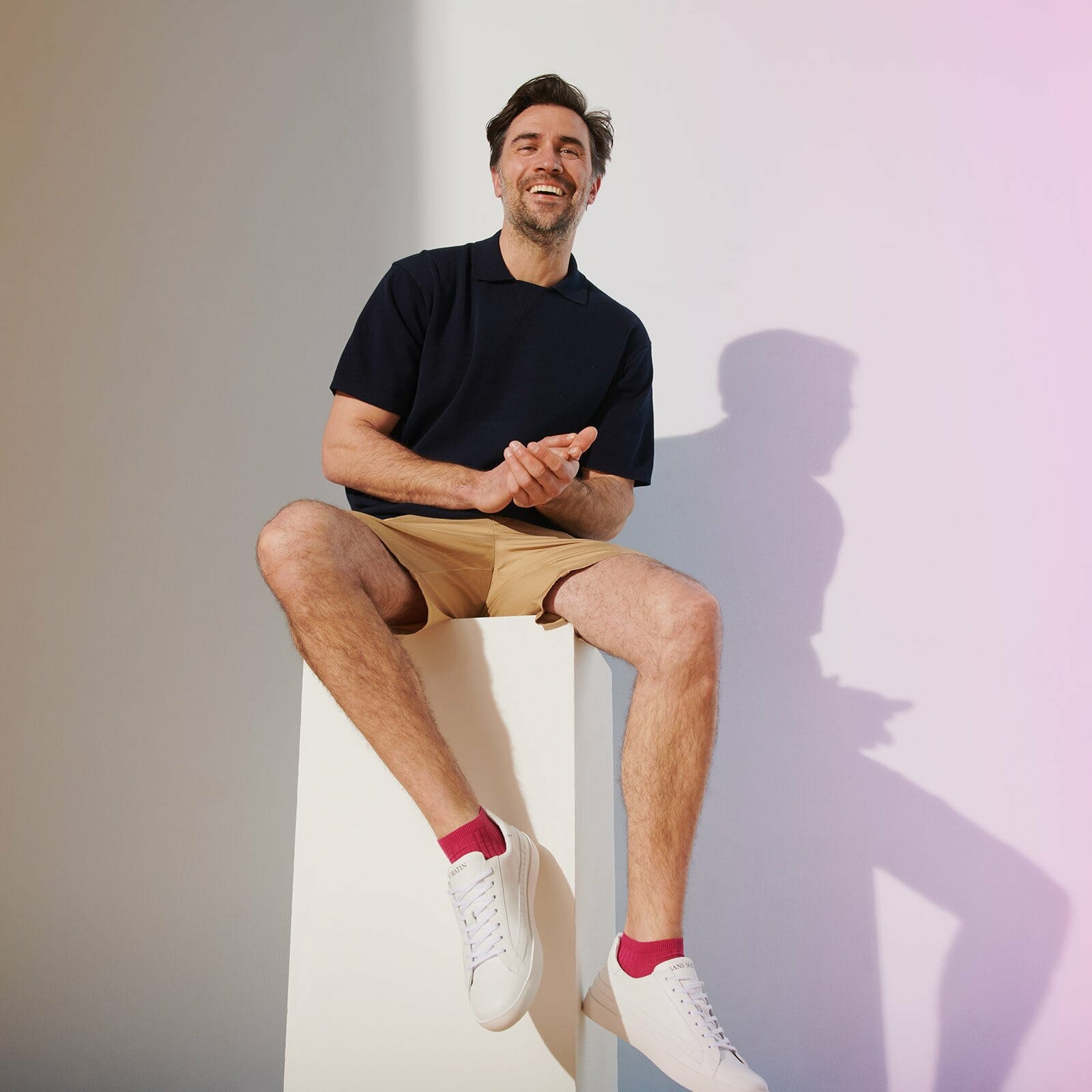 Man in shorts sitting down flashing his pair of fuchsia trainer socks with white trainers.
