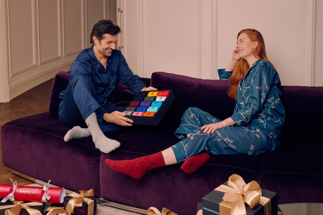 a man and a woman sitting on a sofa, with giant box of socks.
