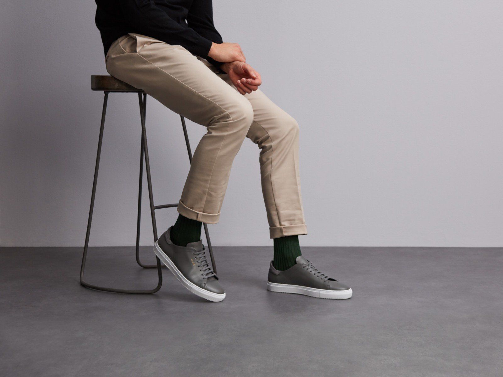 man on chair wearing british racing green socks and chinos with grey leather trainers