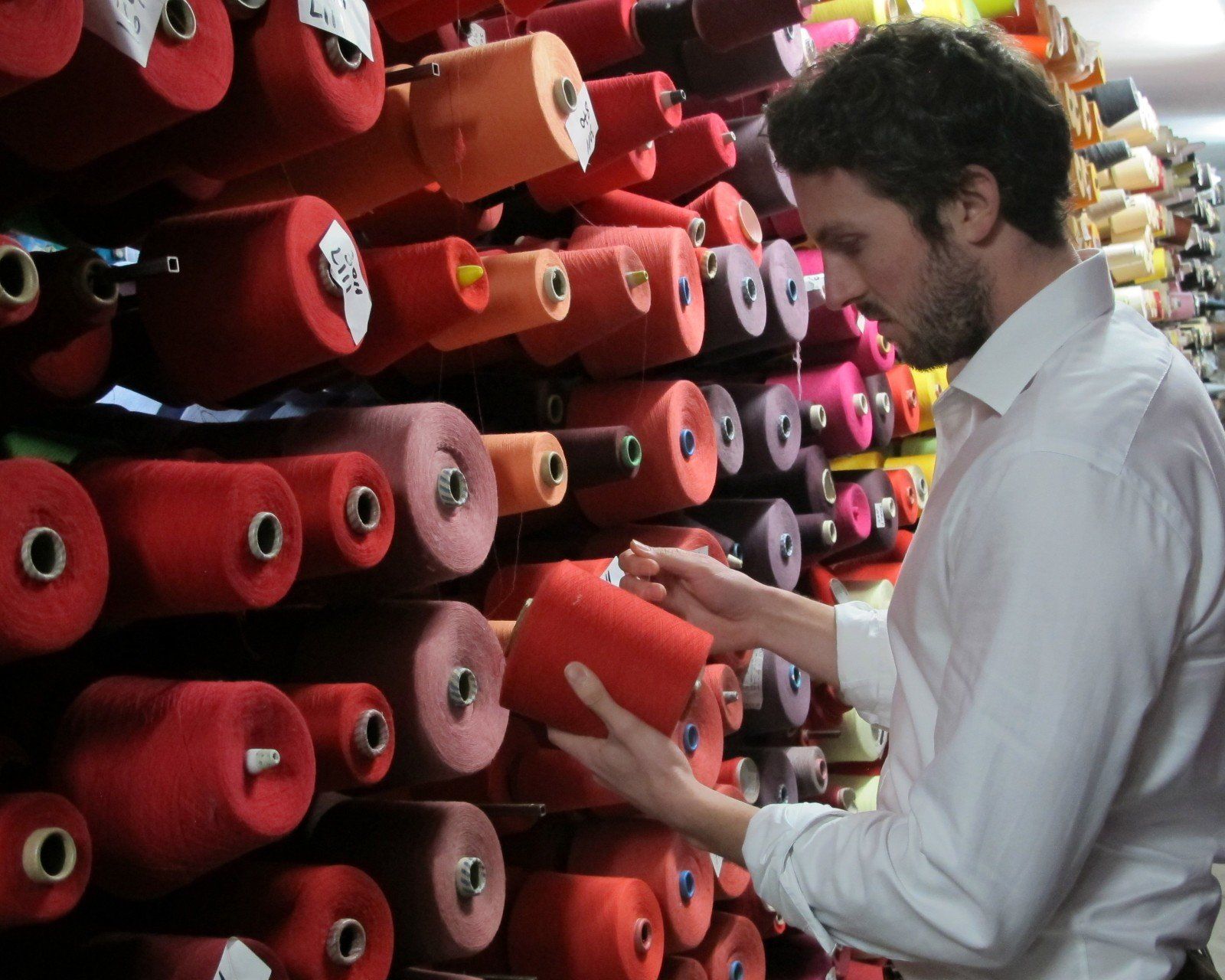 Dave, one of the co-founders, examines multiple red yarn spools in a factory