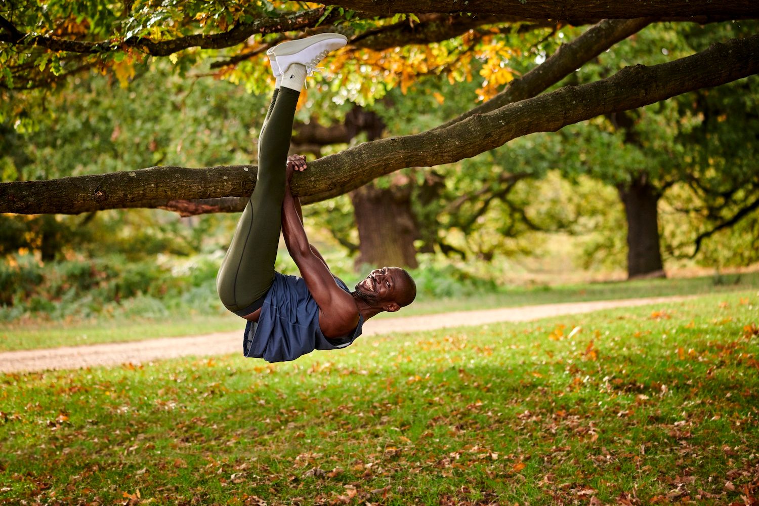 A man hangs smiling upside down from a tree branch, enjoying his exercise outdoors in London Sock Company sports socks