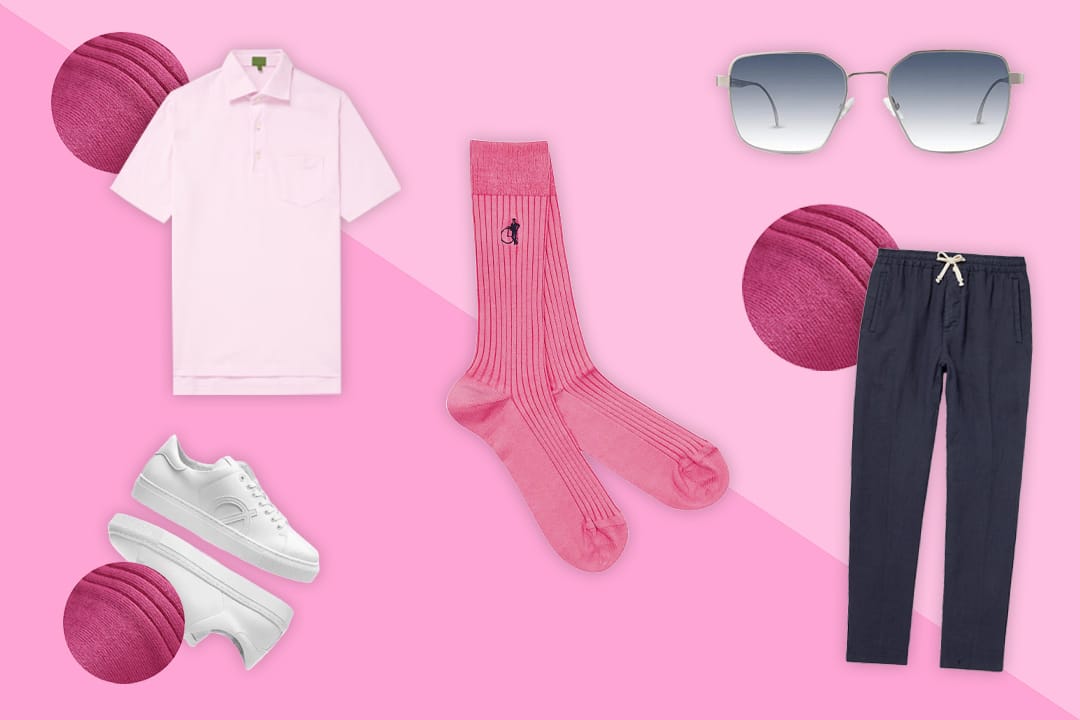 Items of men's clothing on a pink background showing how to style plain pink socks, including a pastel pink polo, white sneakers, and navy drawstring trousers.
