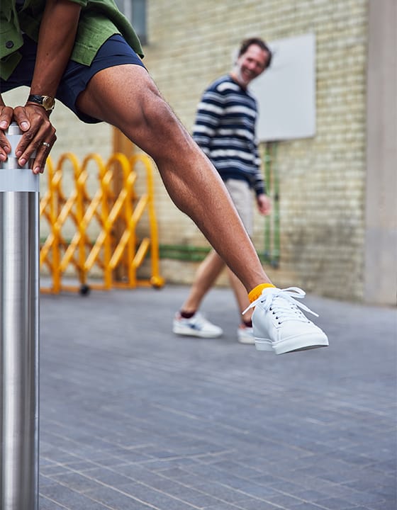 A man jumping over metal bollard wearing navy shorts, saffron yellow trainer socks and white trainers.