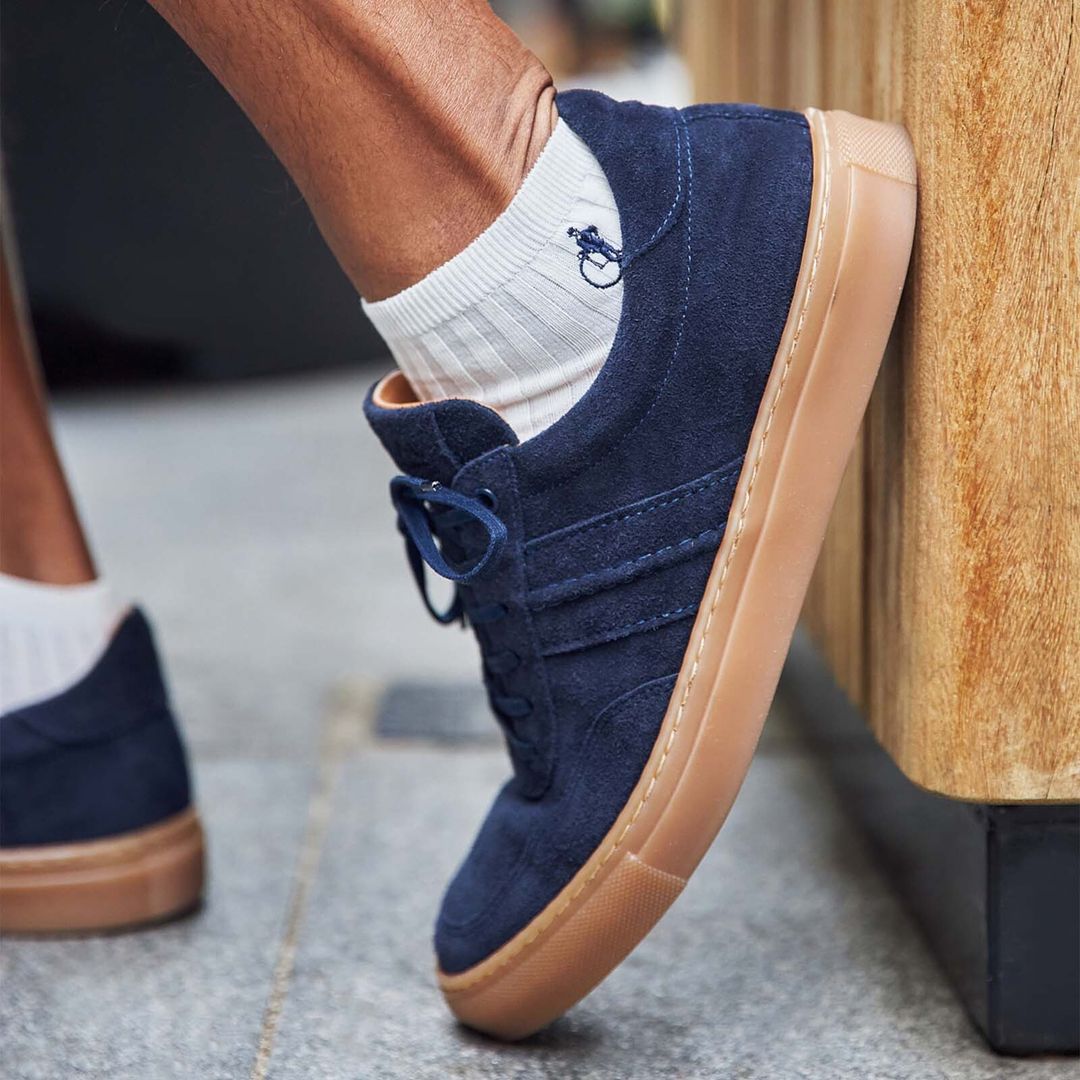 A close up shot of a pair of men’s feet in plain white trainer socks and navy blue suede trainers.