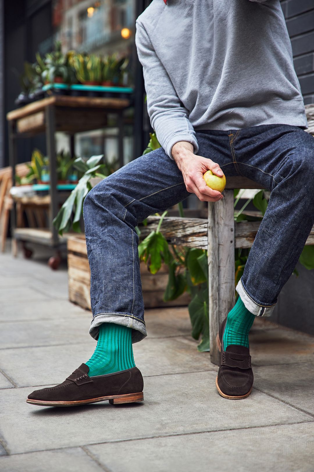 Man sitting on the edge of a wooden bench with emerald green sartorial socks