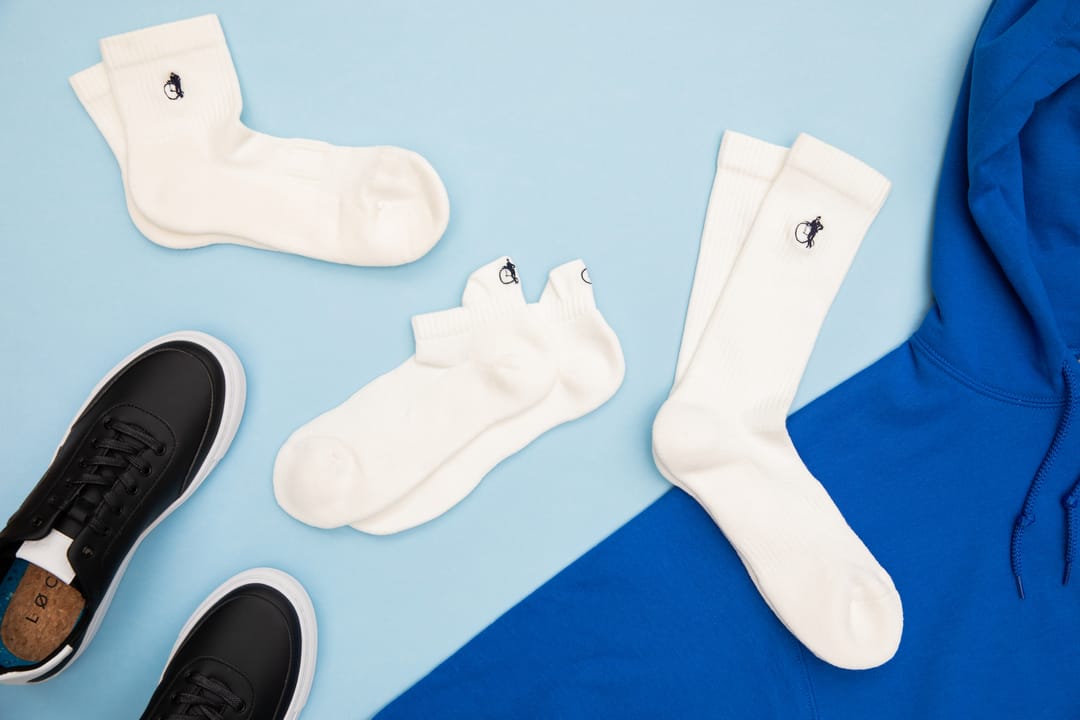 Three pairs of white sports socks in different lengths lay on a blue background beside a blue hoody and black trainers.