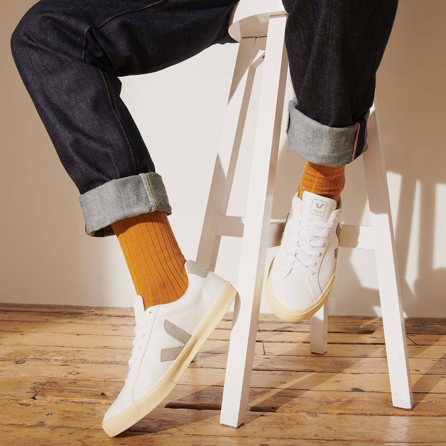 Man sitting on white stool in black denim jeans, saffron socks and paired with white trainers