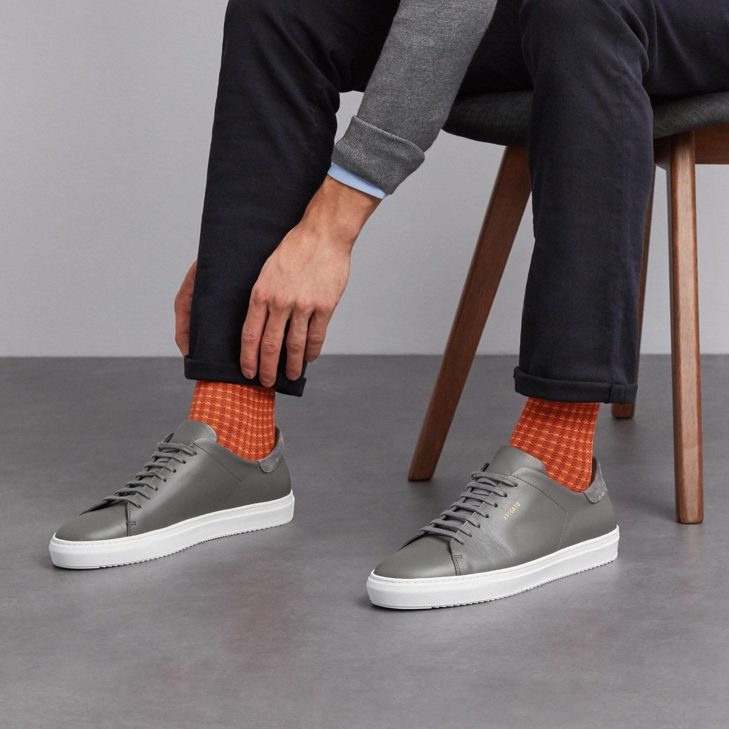 Man sitting and touching the cuff of his trousers wearing orange chequered socks