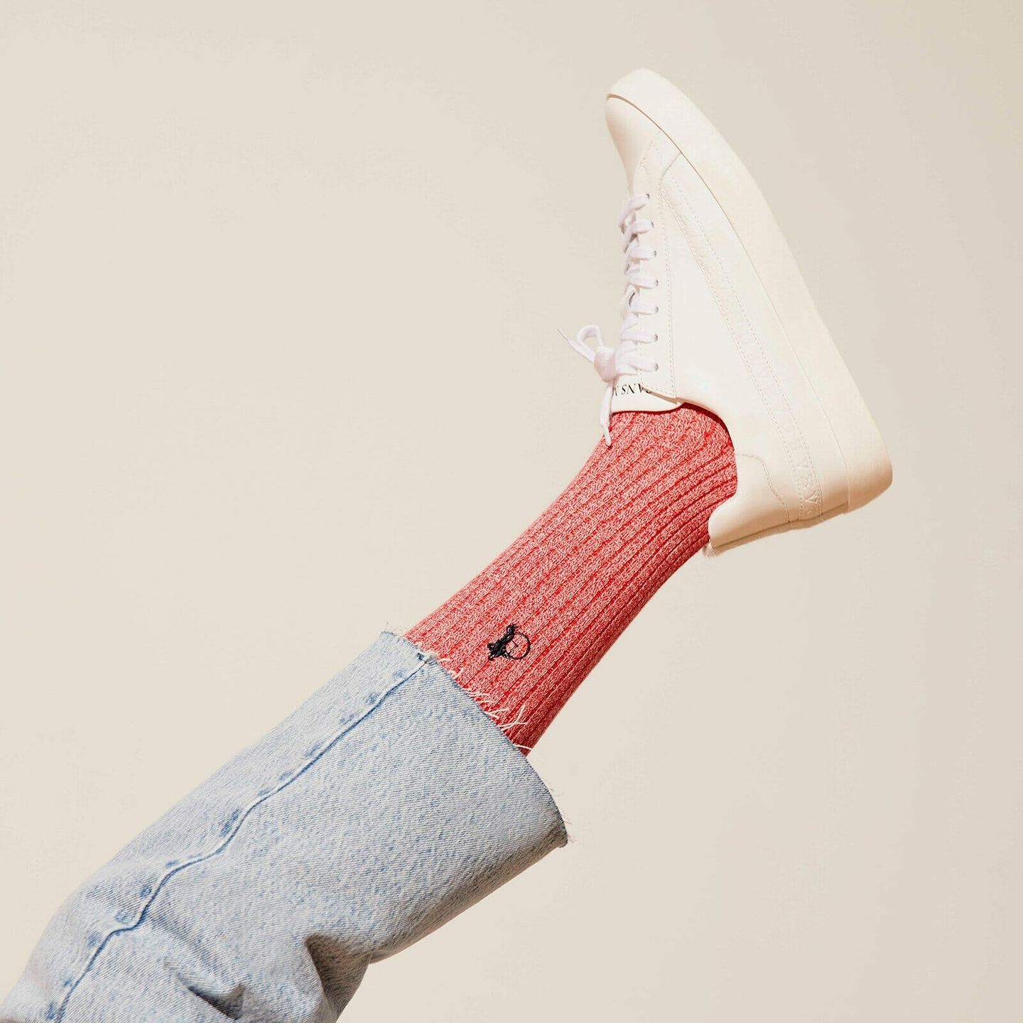 A leg extended into the air, with a Marl Red sock, white trainer and light blue
