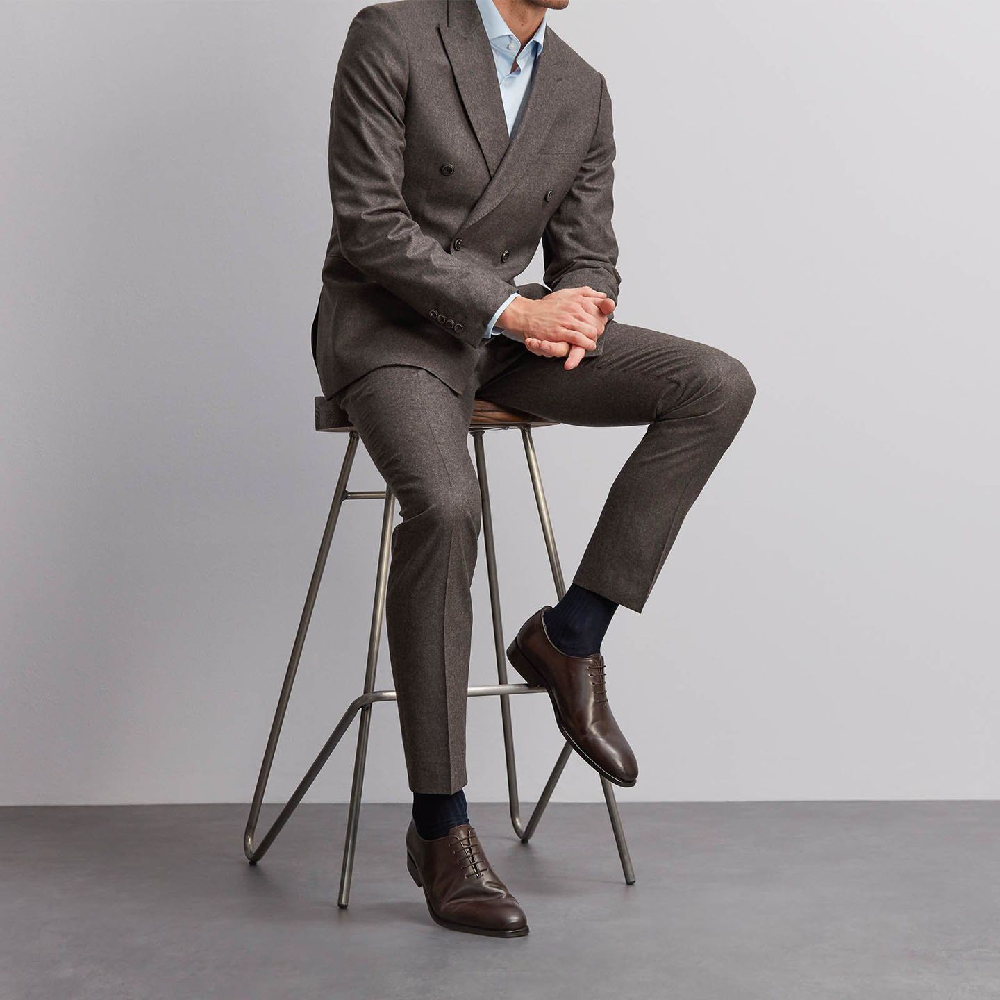Man sitting on a stool wearing a dark grey double breasted suit and navy sartorial socks