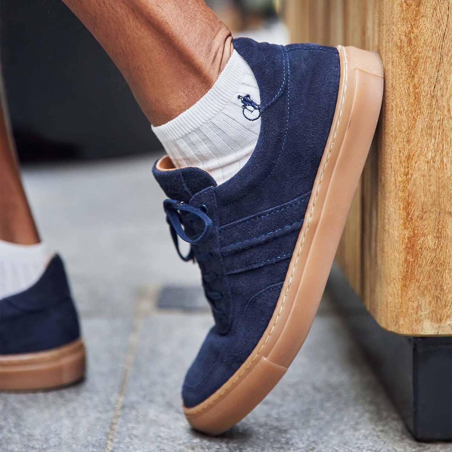 A close up shot of a pair of feet in white trainer socks and navy blue suede trainers