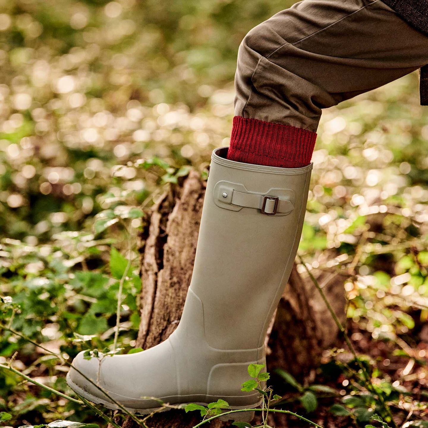 A man standing on a bark of wood in a forest, wearing off white wellies and red boot socks