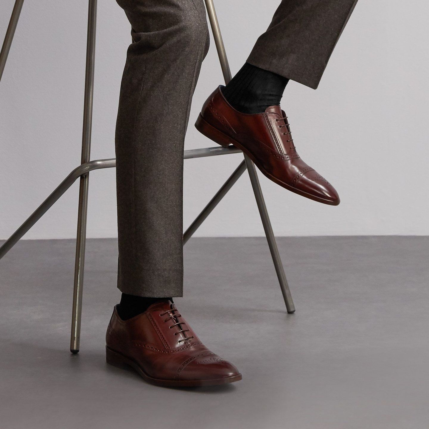 A close up of someone wearing dark grey socks with smart brown shoes