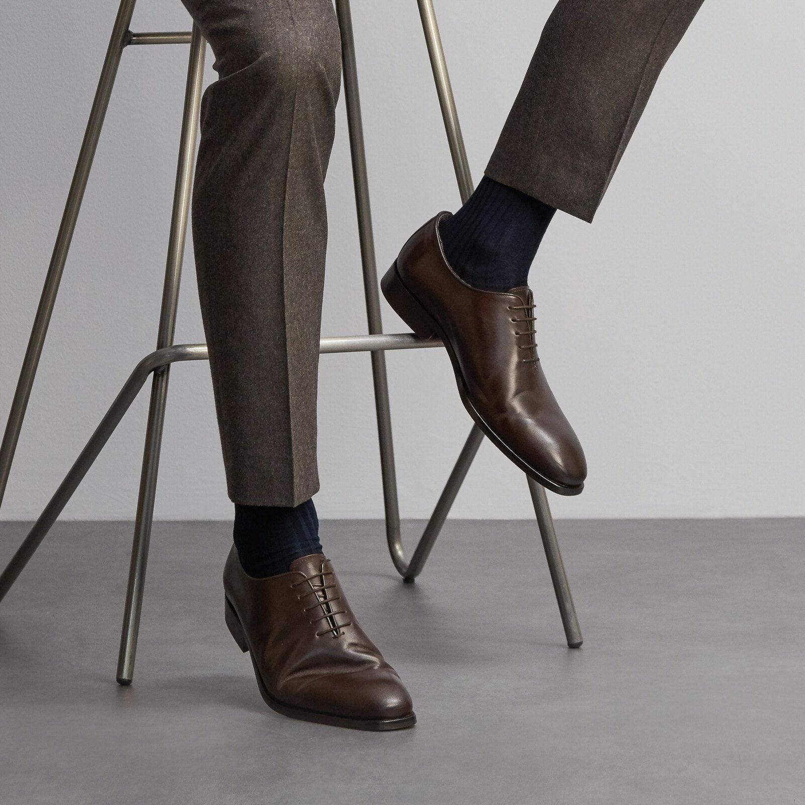 Close up of a man sitting on a stool wearing a dark grey suit and navy cotton socks